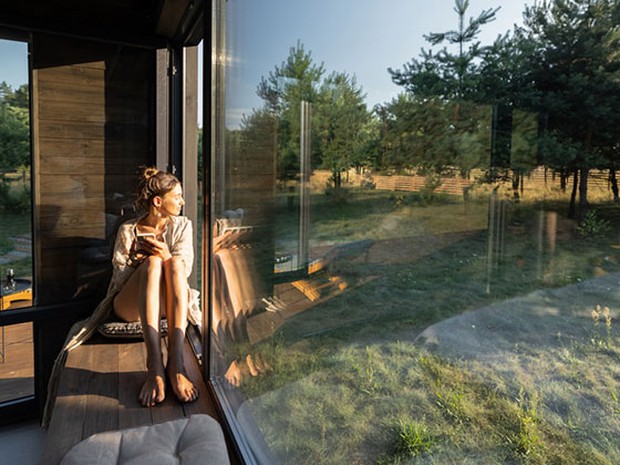 Een vrouw die tegen het raam aanzit in de zon uitkijkend op de natuur