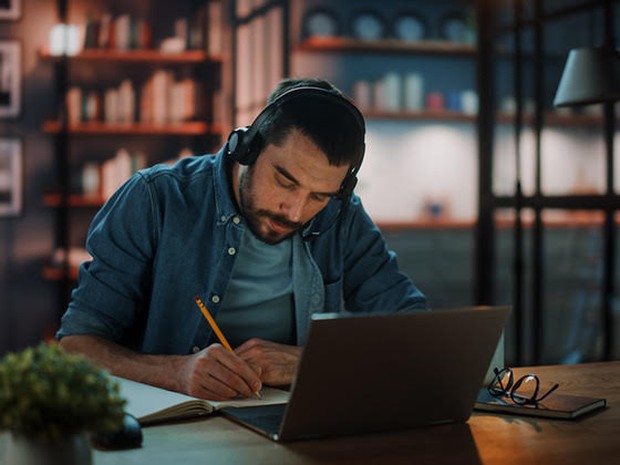 Man met koptelefoon studeert achter laptop