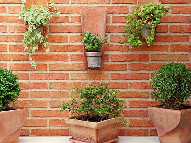 staande en hangende terracotta potten met planten op bakstenen muur