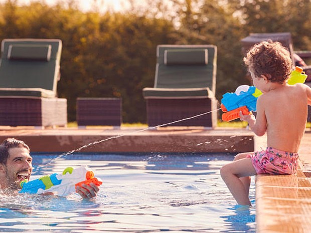 Een vader en zoon in een zwembad spelend met waterpistolen