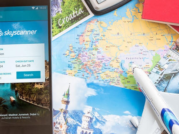 Paspoorten, vakantiefoto's, de wereldkaart en mobiel met Skyscanner app op tafel