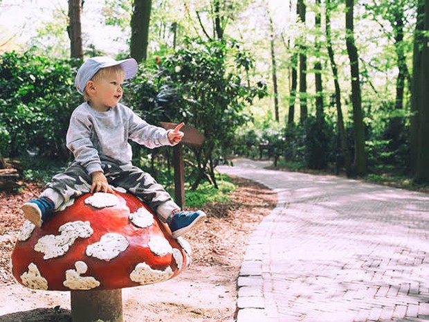 Een jongetje die op een grote nep paddenstoel zit in een pretpark