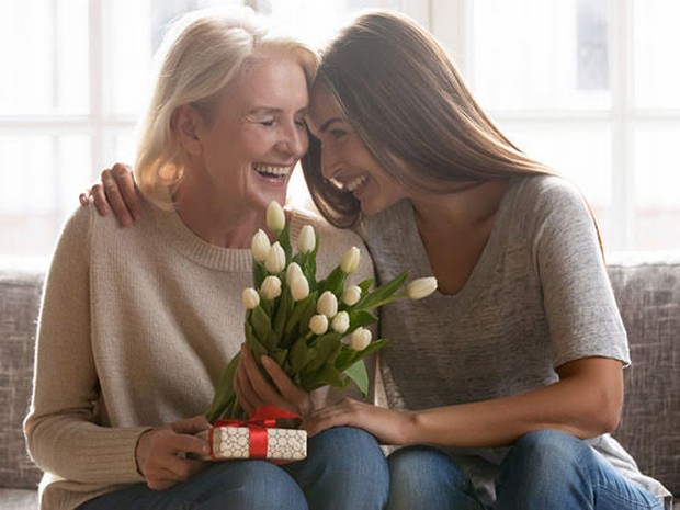 Een dochter die haar moeder op de bank een bos tulpen en ander cadeautje heeft gegeven