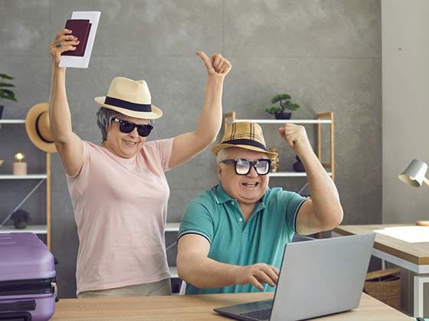 Een blij senior echtpaar in vakantie outfit achter de laptop