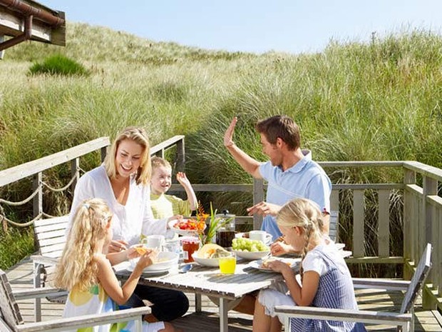 Een gezin dat voor een vakantiehuisje in de duinen eet